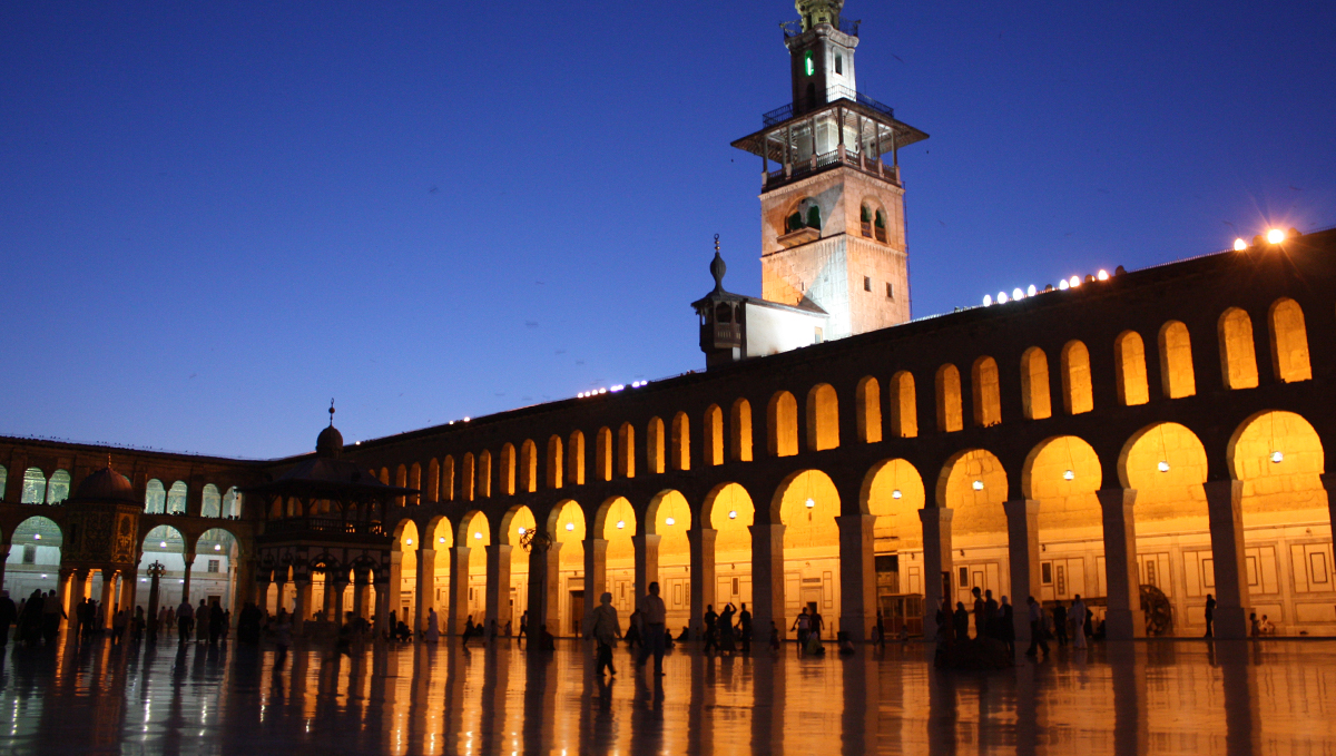 People walking through interior courtyard of large mosque in Damascus, Syria at dusk.