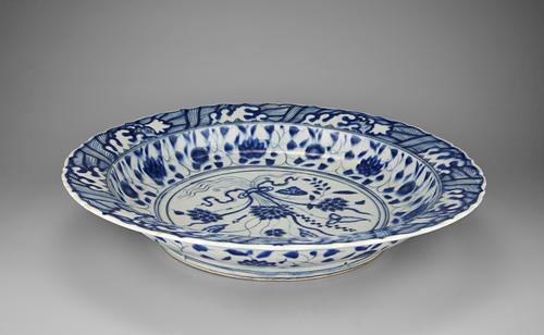 Side view of the blue and white dish that follows a Chinese model so closely that it might have passed for a Chinese original if the body had been translucent like porcelain. Blue and white designs cover the white plate with a foliage design in the centre.