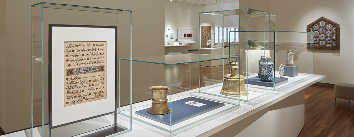 Museum collection gallery, featuring multiple objects on a large rectangular showcase under four glass top covers.