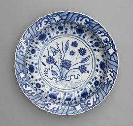 Blue and white dish with sloping foliate rim, in the centre a lotus bouquet tied with a ribbon.